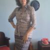 Vestido chemisier vintage original dos anos 70 na cor branca com estampa geométrica azul marinho. Modelo midi com mangas longas, fechamento frontal por botões e faixa para amarração na cintura. Peça vintage feminina em excelente estado de conservação, fotografada em ambiente interno com decoração retrô.