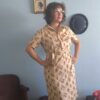 Vestido chemisier vintage original dos anos 70 em tom bege com estampa geométrica retrô em tons terrosos e alaranjados. Modelo midi com mangas curtas, fechamento frontal por botões e faixa para amarração na cintura. Peça feminina vintage em excelente estado de conservação, fotografada em ambiente interno com decoração retrô.