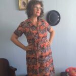 Chemisier vintage original dos anos 70 em jersey de poliamida com estampa floral em tons coral, marrom e bege. Modelo midi com mangas curtas, fechamento frontal por botões e faixa para amarração na cintura. Peça feminina vintage em excelente estado de conservação, fotografada em ambiente interno com decoração retrô.