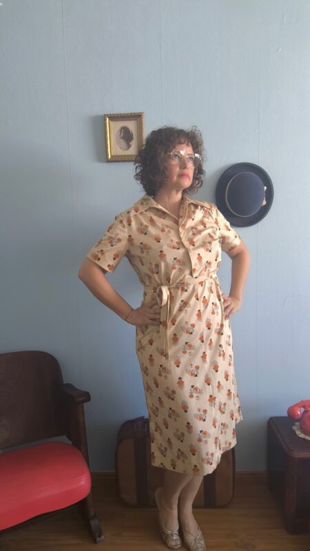 Vestido chemisier vintage original dos anos 70 em tom bege com estampa geométrica retrô em tons terrosos e alaranjados. Modelo midi com mangas curtas, fechamento frontal por botões e faixa para amarração na cintura. Peça feminina vintage em excelente estado de conservação, fotografada em ambiente interno com decoração retrô.