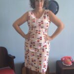 Vestido vintage original dos anos 70 com fundo claro e estampa geométrica colorida em azul-marinho, vermelho, amarelo e rosa. Modelo sem mangas, comprimento midi e corte reto. Peça feminina vintage em tecido sintético, sem forro, fotografada em ambiente interno com decoração retrô.