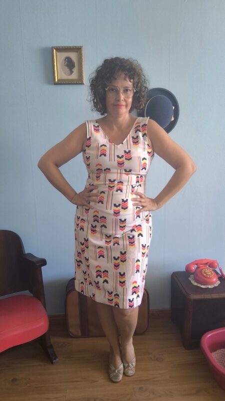 Vestido vintage original dos anos 70 com fundo claro e estampa geométrica colorida em azul-marinho, vermelho, amarelo e rosa. Modelo sem mangas, comprimento midi e corte reto. Peça feminina vintage em tecido sintético, sem forro, fotografada em ambiente interno com decoração retrô.