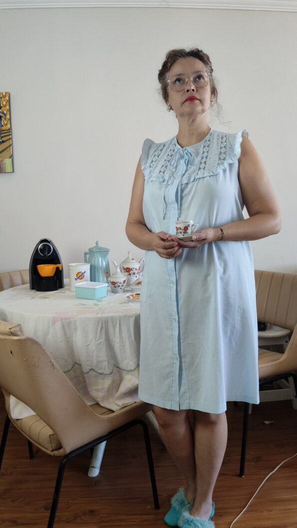 mulher usando Camisola vintage provável anos 80 em azul-claro, usada em modelo, com ampla pala de bordado inglês, babados e fechamento frontal por botões. em frente a mesa com café da manhã, louças vintage.