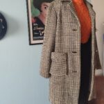 Casaco vintage original dos anos 1970 confeccionado em lã com estampa xadrez Príncipe de Gales, modelagem alongada, lapela clássica e bolsos frontais com lapela.