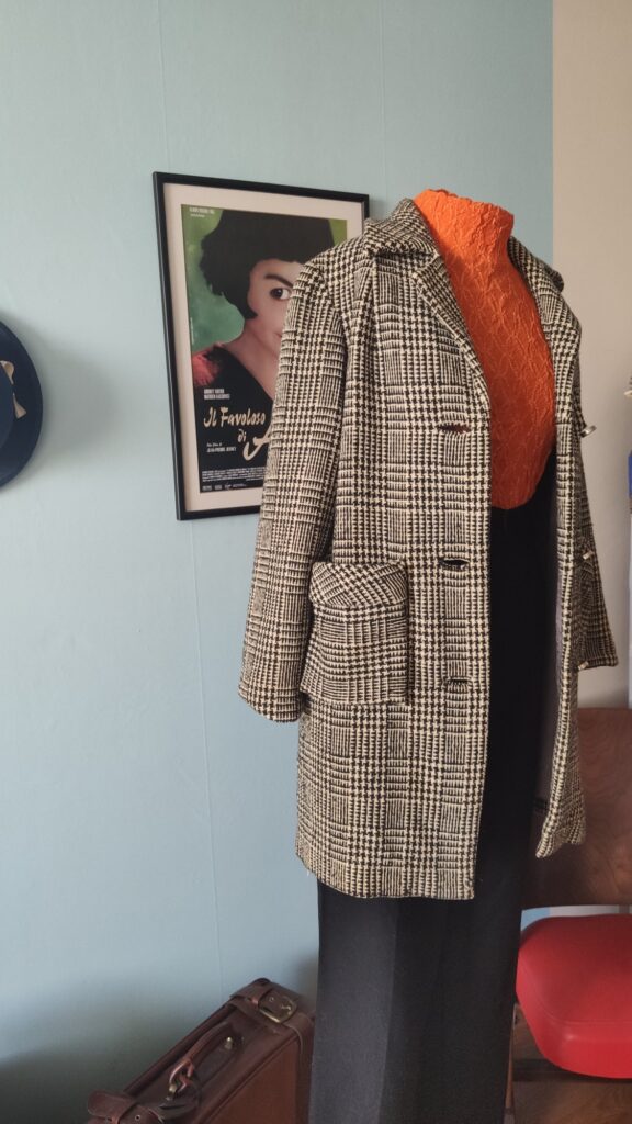 Casaco vintage original dos anos 1970 confeccionado em lã com estampa xadrez Príncipe de Gales, modelagem alongada, lapela clássica e bolsos frontais com lapela.