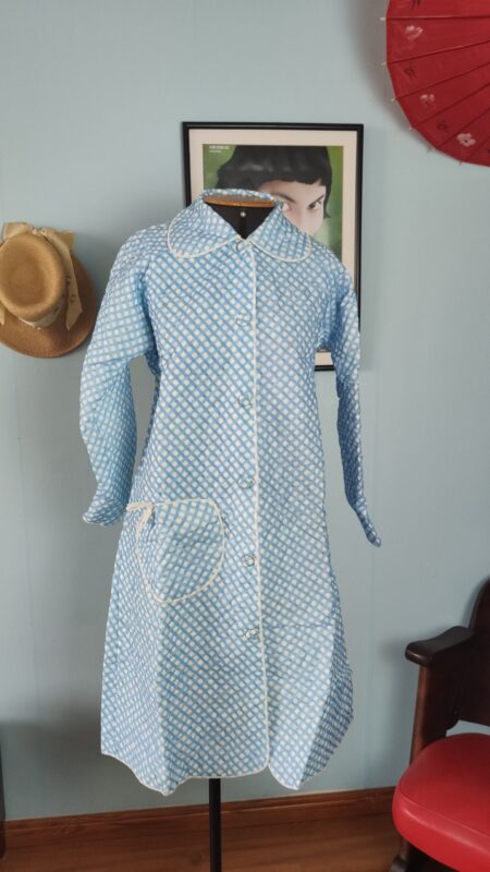 Penhoar vintage original dos anos 70 em azul e branco, com estampa quadriculada, gola arredondada, mangas longas e um bolso frontal.