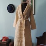 Penhoar vintage Trianon em matelassê creme, longo, com gola xale, mangas compridas e faixa para amarração na cintura.