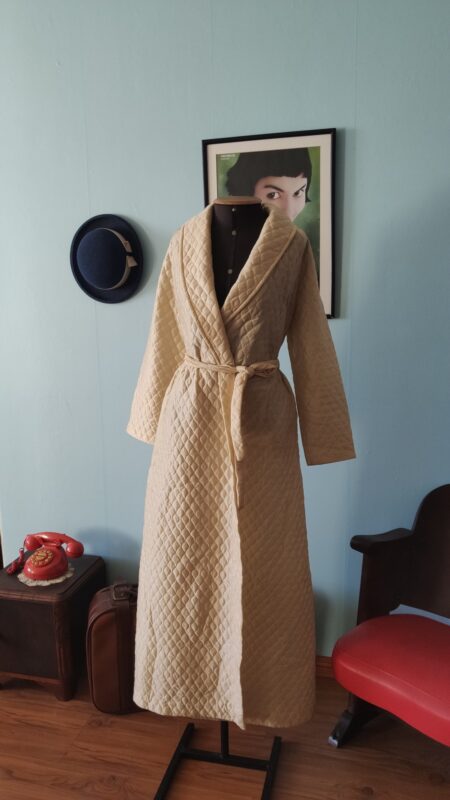 Penhoar vintage Trianon em matelassê creme, longo, com gola xale, mangas compridas e faixa para amarração na cintura.