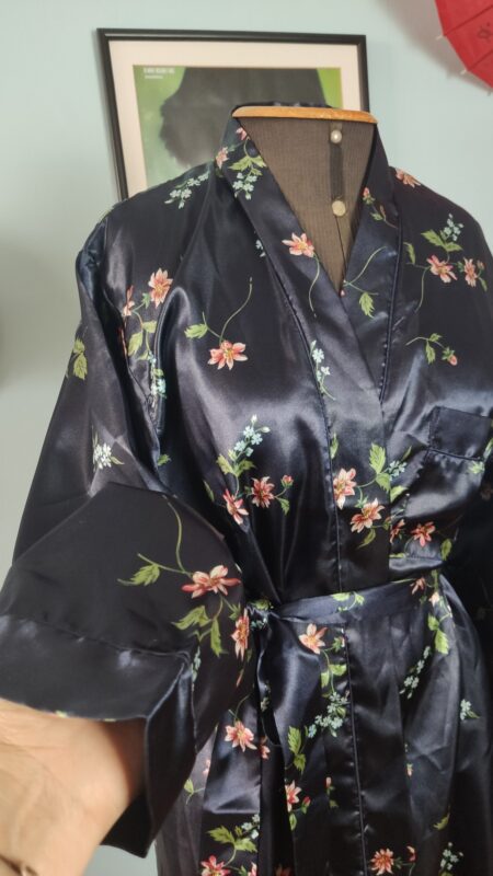 Detalhe frontal de penhoar vintage azul-marinho em cetim floral, mostrando a gola ampla, bolso aplicado e faixa da cintura.