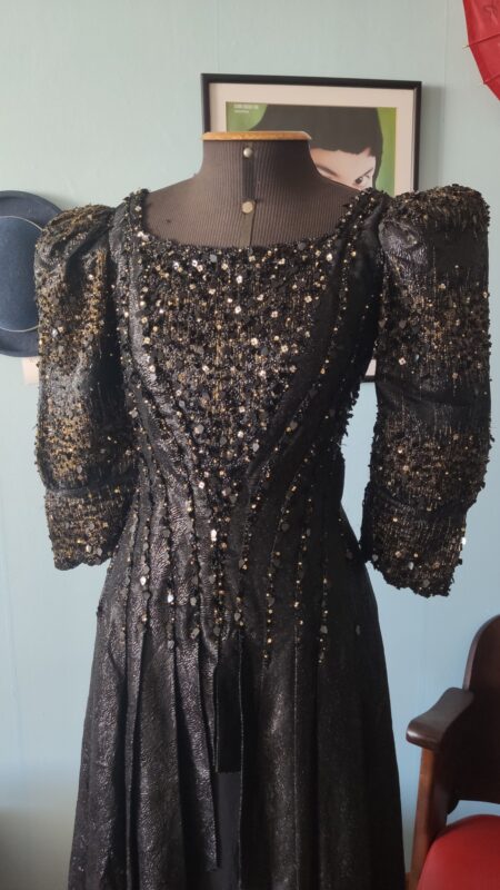 Vestido vintage original dos anos 1980 em lamê brocado preto, com mangas longas volumosas, cintura marcada e bordado ornamental.
