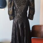Vestido vintage original dos anos 1980 em lamê brocado preto, com mangas longas volumosas, cintura marcada e bordado ornamental.