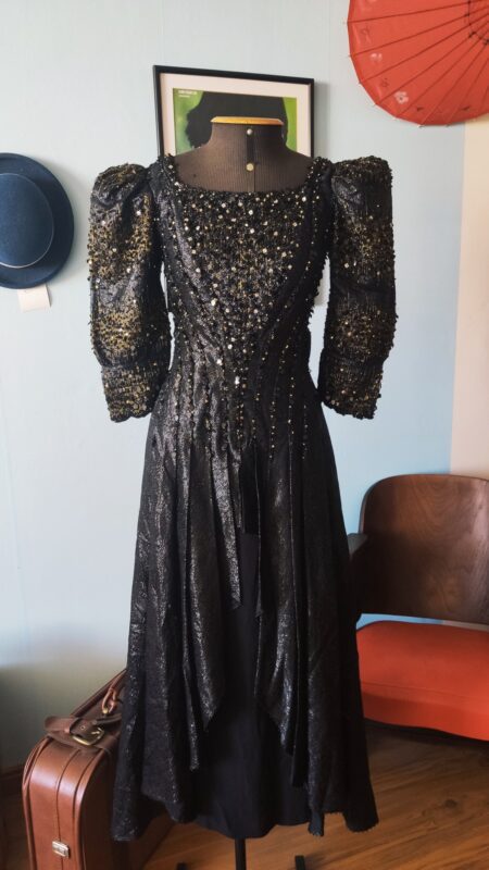 Vestido vintage original dos anos 1980 em lamê brocado preto, com mangas longas volumosas, cintura marcada e bordado ornamental.