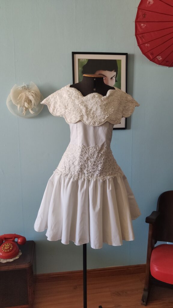 Vestido de festa vintage original dos anos 80 em tafetá branco, exibido em manequim, com gola ornamentada, cintura marcada e saia volumosa.