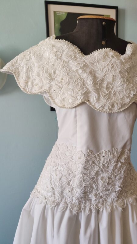 Detalhe de vestido vintage branco dos anos 80 mostrando renda guipir floral aplicada, acabamento com pequenas pérolas e tafetá.