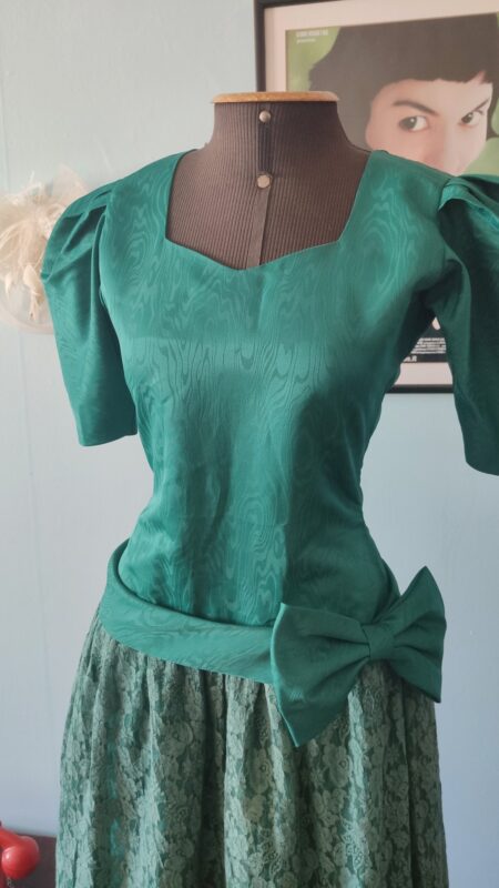 Detalhe do vestido vintage verde anos 80 mostrando o tafetá com textura adamascada, mangas estruturadas, cintura marcada e grande laço lateral.