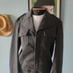 Jaqueta militar vintage cinza chumbo em lã 100%, com lapelas largas, bolsos no peito e modelagem curta.