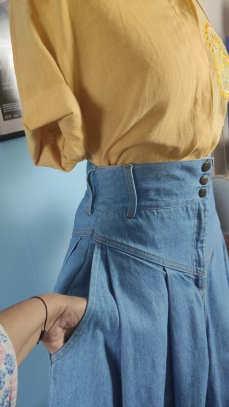Detalhe do cós alto da saia jeans vintage dos anos 80, com três botões laterais, passantes e bolso lateral.
