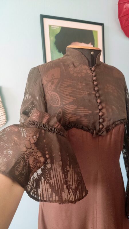 Detalhe do vestido vintage marrom dos anos 60 mostrando gola alta, botões revestidos e tecido devorê na parte superior.