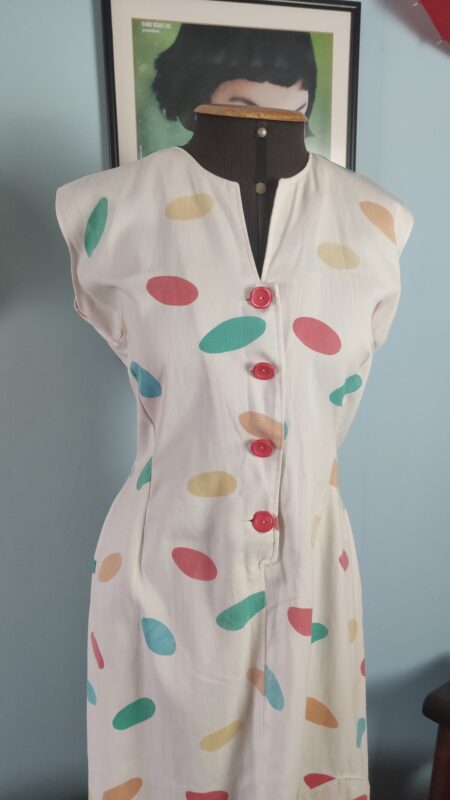 Detalhe frontal de vestido vintage de algodão, mostrando os botões vermelhos, a estampa geométrica colorida e a modelagem ajustada.