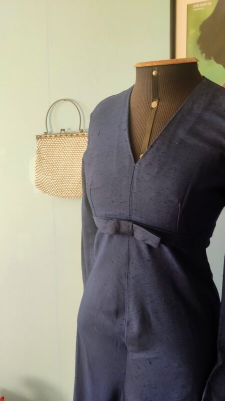 Detalhe do corpo do vestido vintage anos 60 em shantung de rayon, destacando o decote V, o laço aplicado na cintura e a textura do tecido.