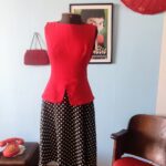 Vestido contemporâneo PA Concept com corpete vermelho sem mangas, cintura marcada com abas peplum e saia preta ampla estampada com poás claros.