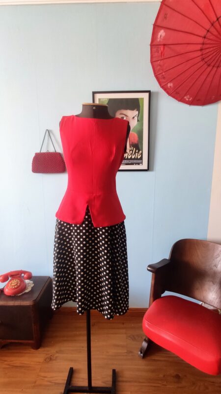 Vestido contemporâneo PA Concept com corpete vermelho sem mangas, cintura marcada com abas peplum e saia preta ampla estampada com poás claros.