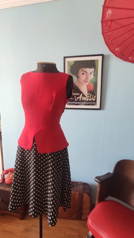 Vestido feminino contemporâneo com corpete vermelho estruturado e saia preta de poás claros, exibido em manequim, com modelagem acinturada e inspiração retrô.