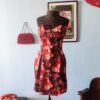 Vestido feminino sem alças, com estampa de flores vermelhas e rosadas sobre fundo escuro, busto estruturado e saia curta levemente evasê, exibido em manequim.